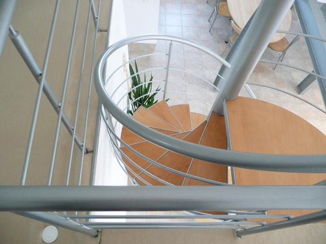 Spiral staircase with light wood treads and a steel railing, seen from above
